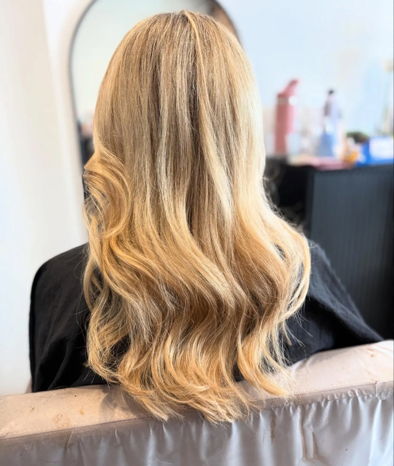 Rear view after: long honey blonde with soft waves and an even, blended tone.