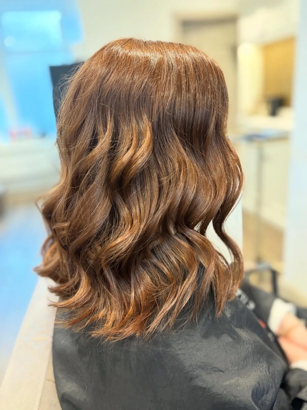Rear view after: rich chestnut with caramel through the mid-lengths, waved.