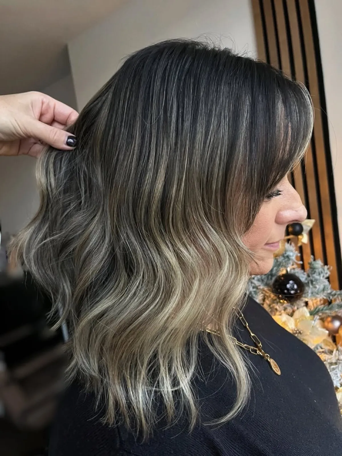 Side view after: a cool ash blonde balayage on a deep base, waved through a soft lob.