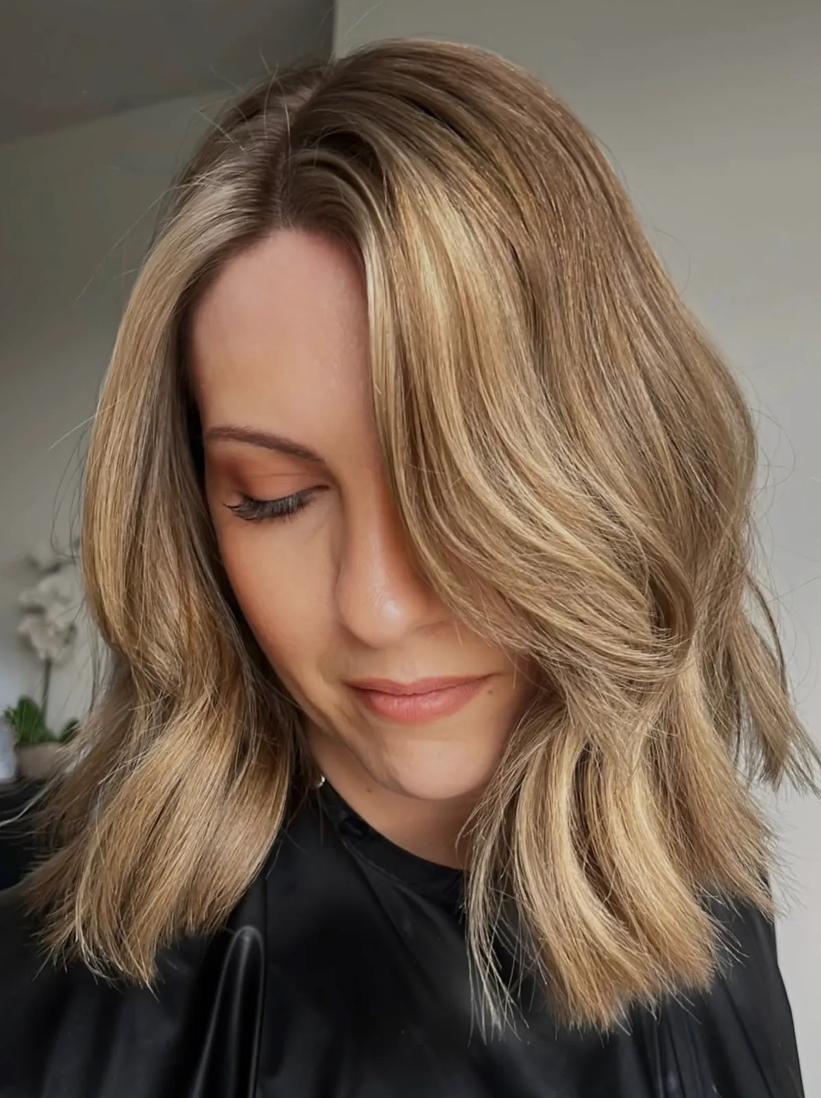 Soft lived-in blonde balayage with a loose wave, styled to the side.