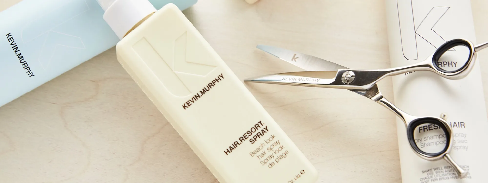 Kevin Murphy Hair Resort beach spray and a pair of Kevin Murphy scissors on light wood.