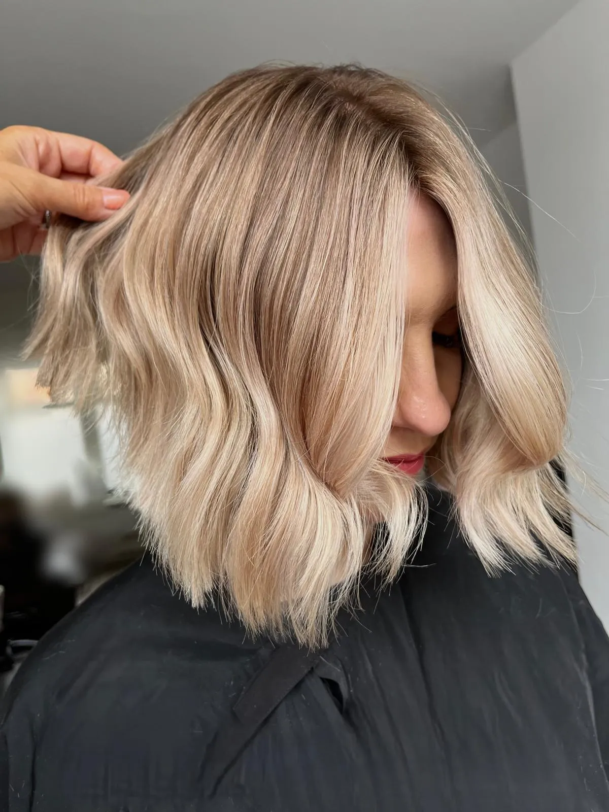 Side view of a chin-length blonde bob with soft waves, hand lifting strands to show texture.