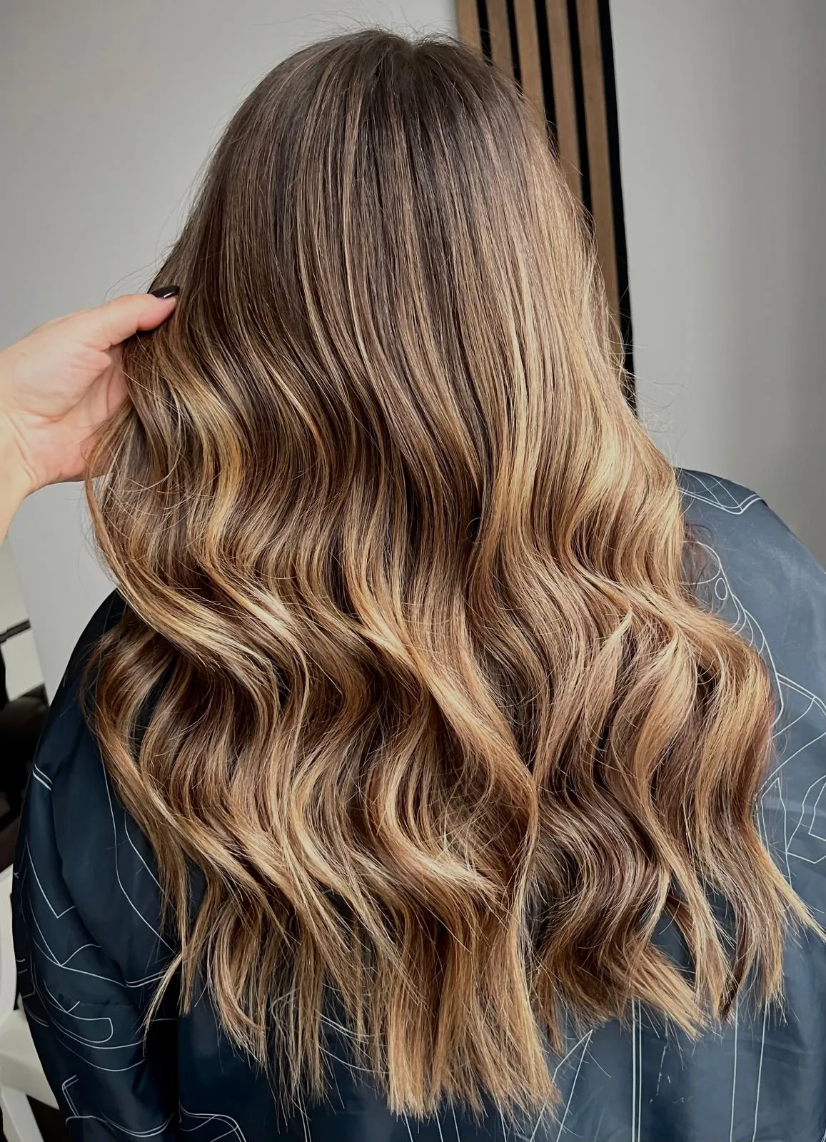 Rear view of long brunette hair with caramel balayage and soft waves.